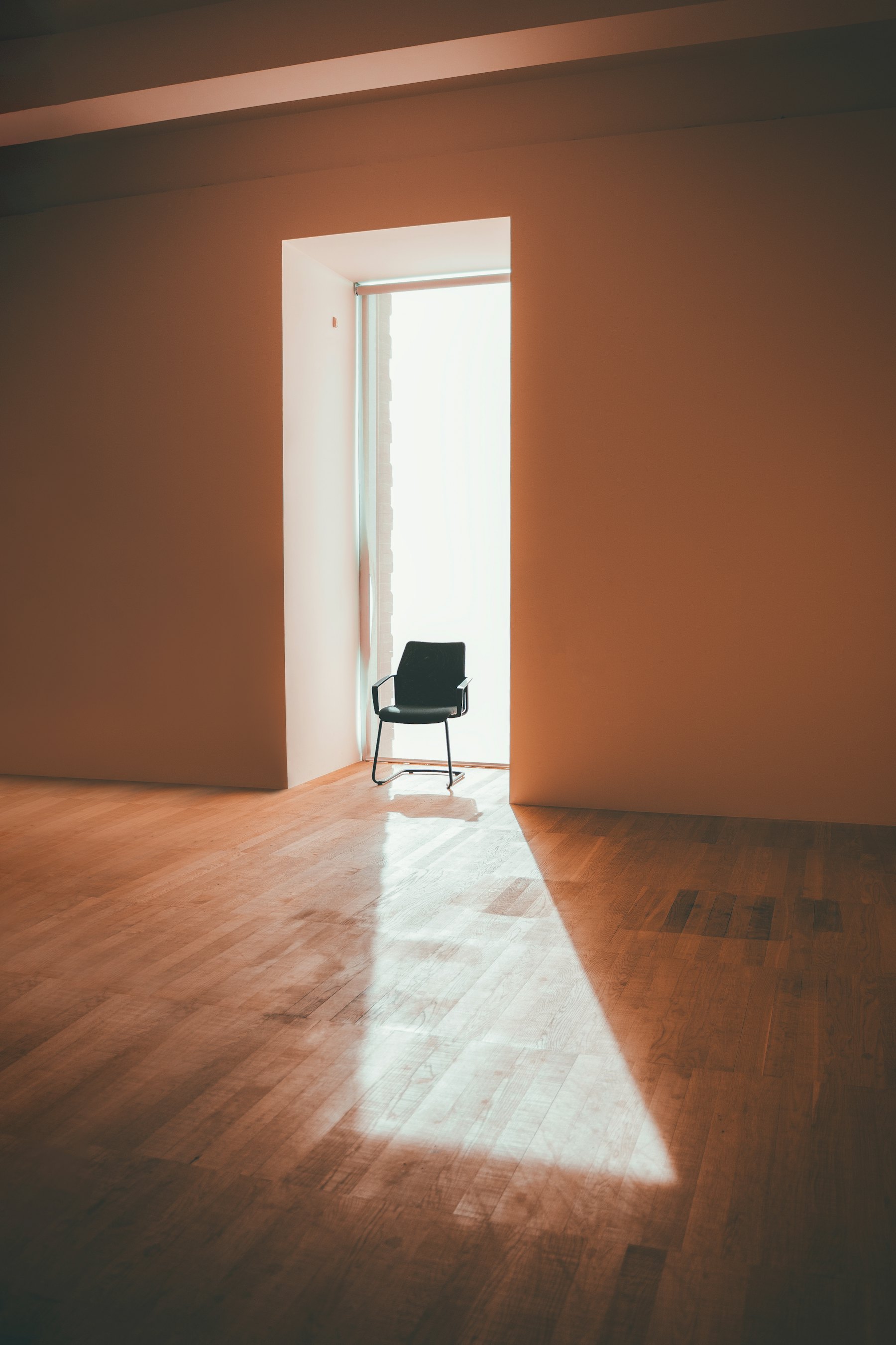 Ein einzelner Stuhl steht in einer hellen Türöffnung, Licht fällt über den Holzboden.
